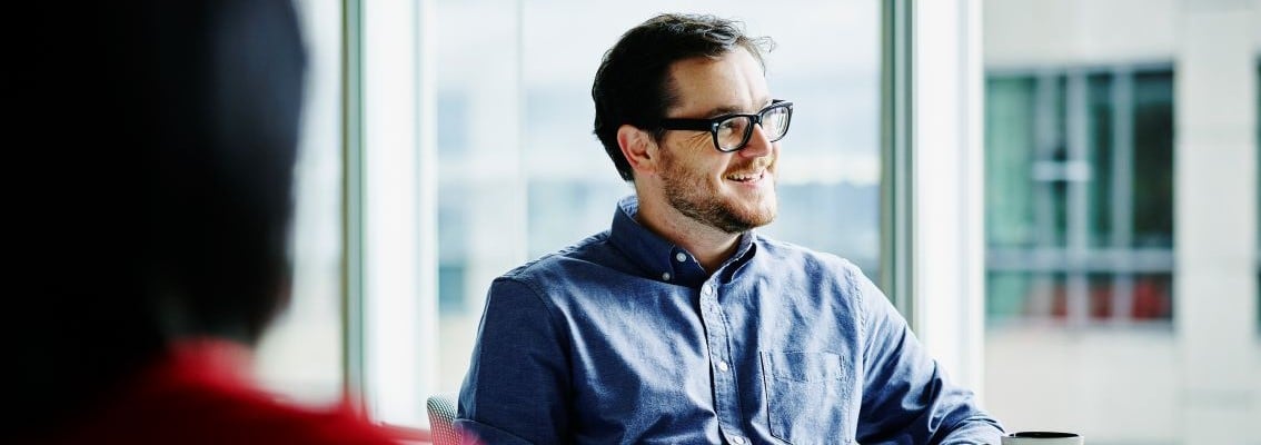 Smiling businessman sitting in meeting with coworkers 1134x400